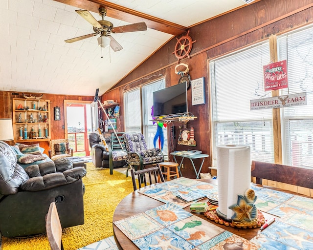 carpeted dining space featuring lofted ceiling with beams, a ceiling fan, and wooden walls