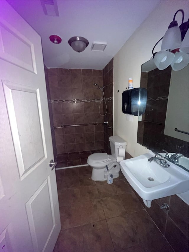 bathroom with toilet, tile patterned flooring, a sink, and tiled shower