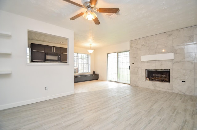 unfurnished living room featuring visible vents, a ceiling fan, light wood-type flooring, baseboards, and a tile fireplace