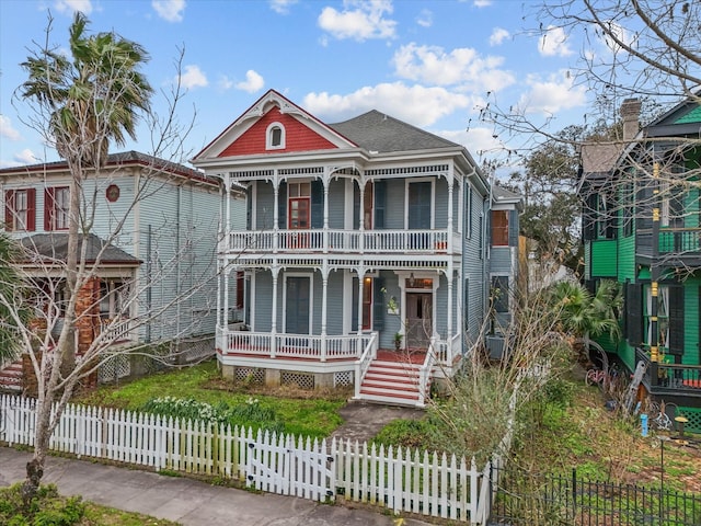 victorian home with a balcony, covered porch, and a fenced front yard