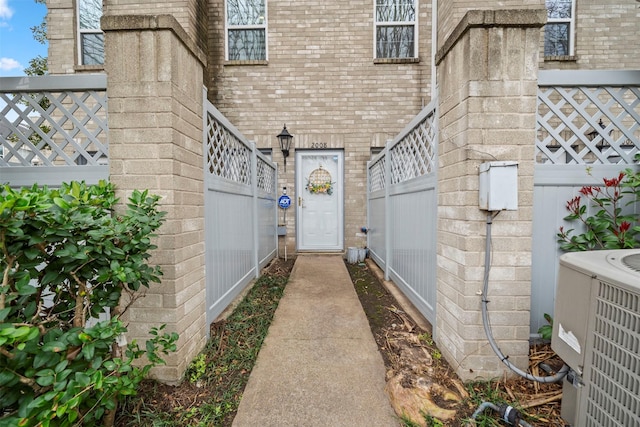 entrance to property featuring central AC, brick siding, and fence