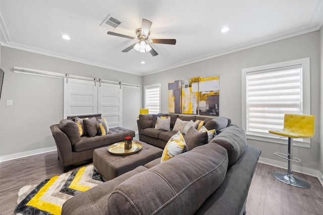 living area with a barn door, dark wood-type flooring, visible vents, baseboards, and crown molding