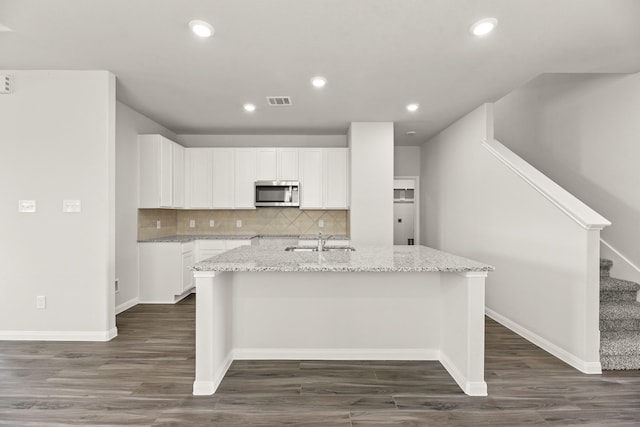 16539 Willow Forest Dr, Conroe, TX 77302 - kitchen with stainless steel microwave, a center island with sink, light stone counters, a sink, and recessed lighting