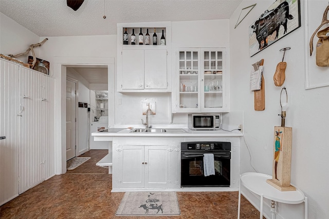 kitchen featuring light countertops, a sink, a textured ceiling, stainless steel microwave, and black oven