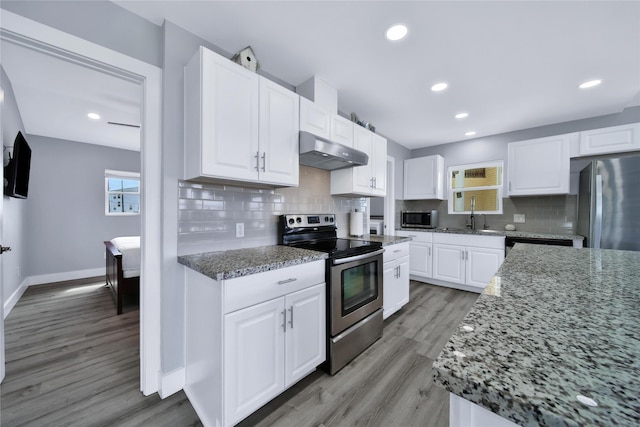 kitchen with white cabinets, under cabinet range hood, light stone counters, and stainless steel appliances