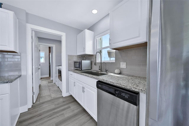 kitchen with appliances with stainless steel finishes, a sink, light stone countertops, white cabinetry, and backsplash