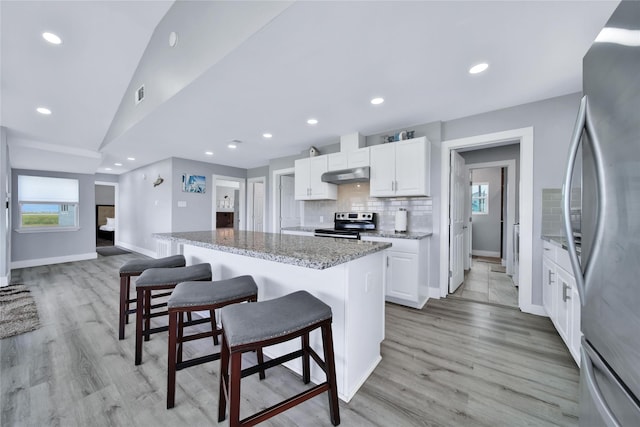 kitchen featuring appliances with stainless steel finishes, a kitchen breakfast bar, a center island, under cabinet range hood, and white cabinetry