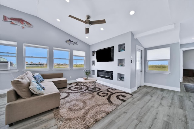 living area featuring light wood-type flooring, lofted ceiling, a glass covered fireplace, and baseboards