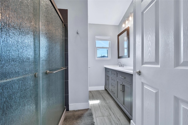 bathroom featuring double vanity, a stall shower, a sink, and baseboards