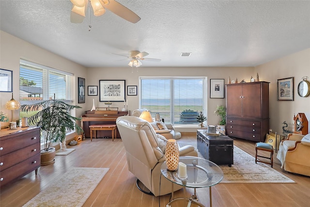 living area with ceiling fan, a textured ceiling, plenty of natural light, and light wood-style flooring