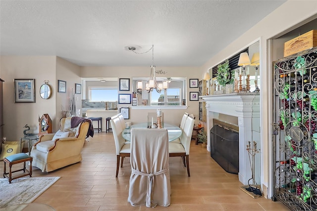 dining room with a glass covered fireplace, a notable chandelier, a textured ceiling, and light wood finished floors