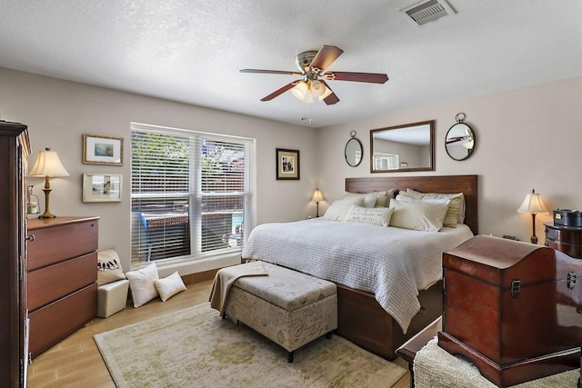 bedroom with a textured ceiling, light wood-style flooring, visible vents, and a ceiling fan