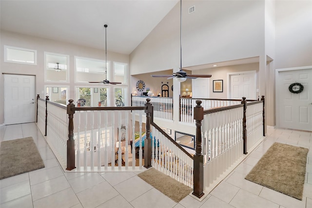 hallway with high vaulted ceiling, light tile patterned floors, visible vents, and an upstairs landing