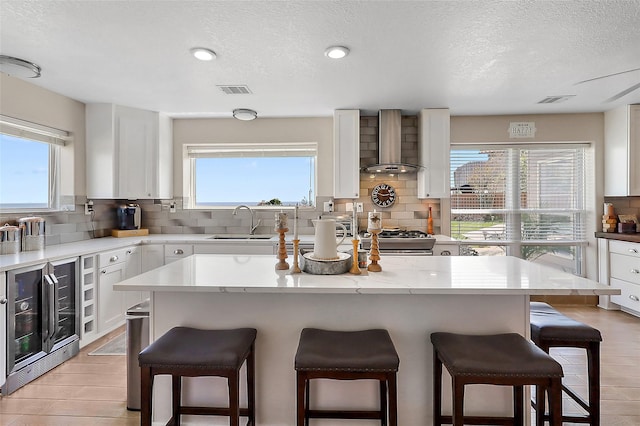 kitchen with wall chimney range hood, a kitchen bar, and wine cooler