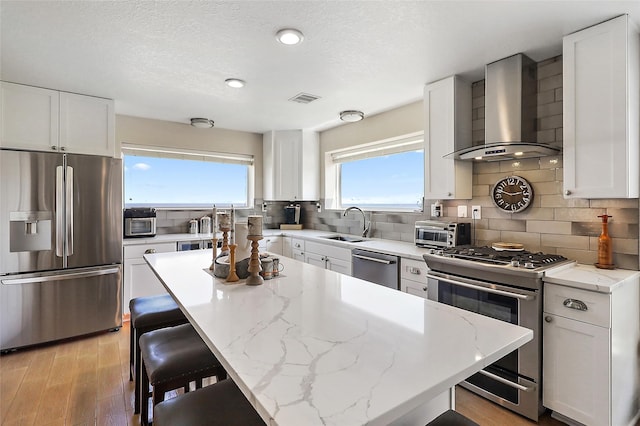 kitchen featuring stainless steel appliances, a center island, white cabinetry, and wall chimney exhaust hood