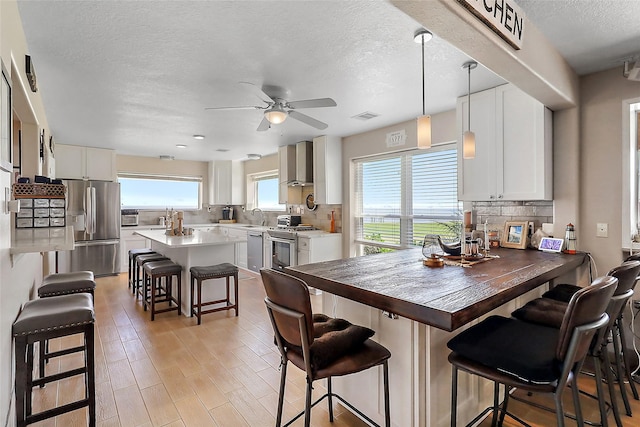 kitchen with a breakfast bar area, appliances with stainless steel finishes, wall chimney range hood, a center island, and decorative light fixtures