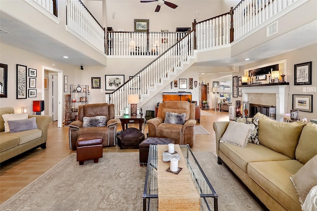 living area with visible vents, light wood-style flooring, a glass covered fireplace, ceiling fan, and stairs