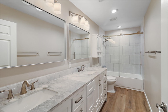 full bathroom with wood finished floors, shower / bath combination with glass door, a sink, and visible vents