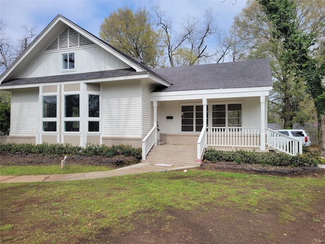 view of front of house with covered porch, a front lawn, and roof with shingles