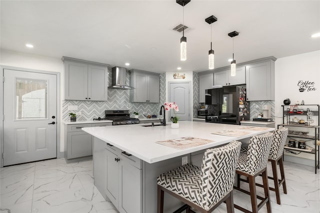 kitchen featuring light countertops, gray cabinetry, stainless steel range oven, a sink, and wall chimney range hood