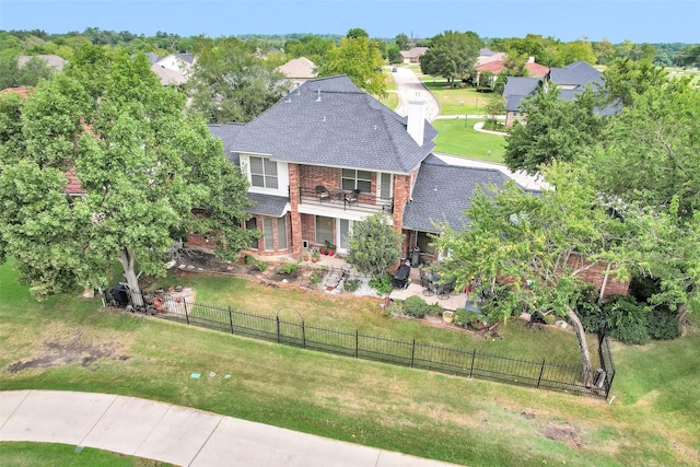 view of front of property with brick siding, a patio, roof with shingles, a fenced backyard, and a front lawn