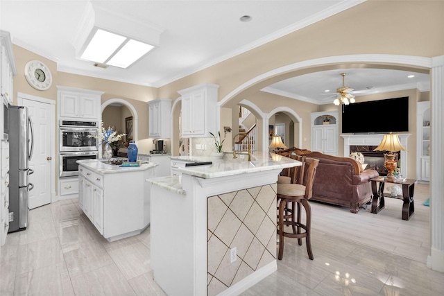 kitchen featuring arched walkways, a peninsula, stainless steel appliances, a kitchen bar, and a high end fireplace