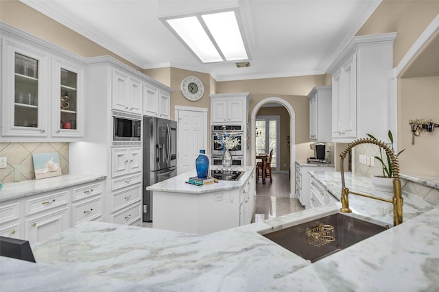 kitchen with arched walkways, decorative backsplash, light stone countertops, stainless steel appliances, and a sink