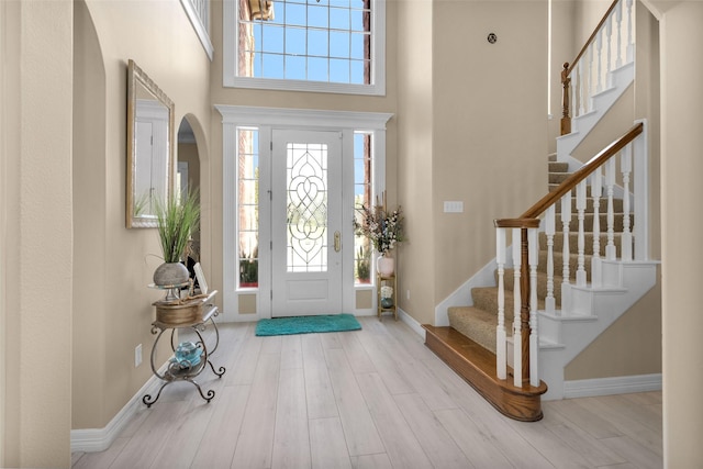 foyer with a towering ceiling, stairway, baseboards, and wood finished floors