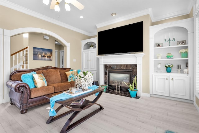 living area featuring a high end fireplace, light wood-type flooring, crown molding, and built in shelves