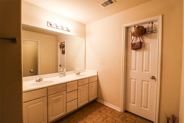 full bathroom featuring a textured ceiling, double vanity, visible vents, and a sink