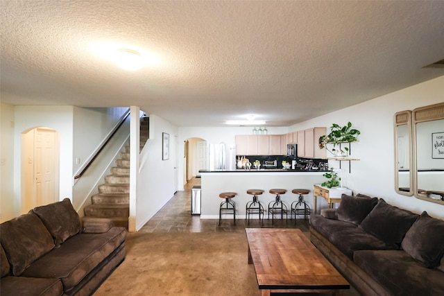 living area featuring stairs, arched walkways, dark carpet, and a textured ceiling