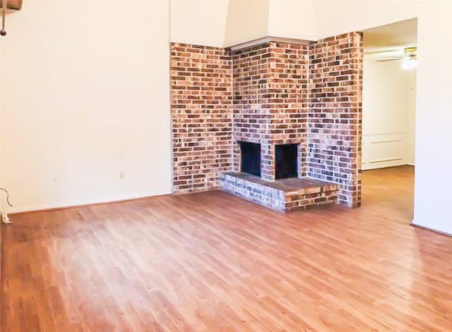 unfurnished living room with a brick fireplace, a ceiling fan, and wood finished floors