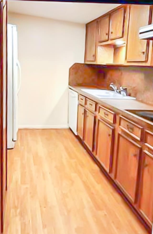 kitchen with white appliances, baseboards, light countertops, light wood-style floors, and a sink