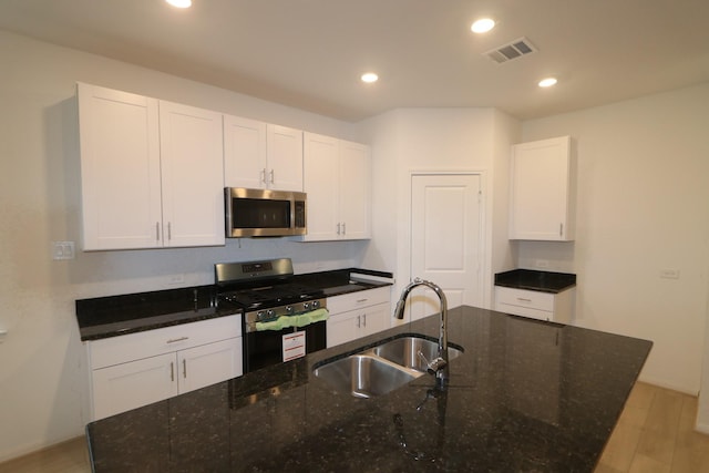 kitchen with stainless steel appliances, a sink, visible vents, white cabinetry, and dark stone countertops