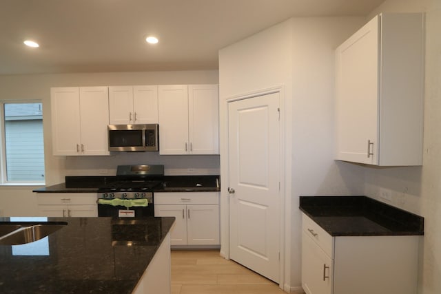 kitchen with recessed lighting, white cabinetry, light wood-style floors, appliances with stainless steel finishes, and dark stone countertops