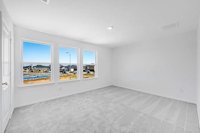 spare room featuring light colored carpet, visible vents, and baseboards