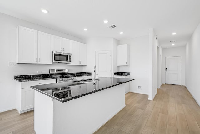 kitchen with visible vents, dark stone countertops, light wood-style floors, stainless steel appliances, and a sink