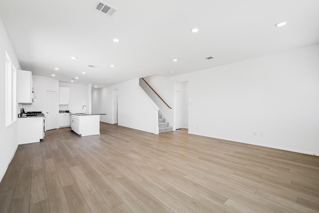 unfurnished living room featuring visible vents, a sink, recessed lighting, light wood finished floors, and stairs