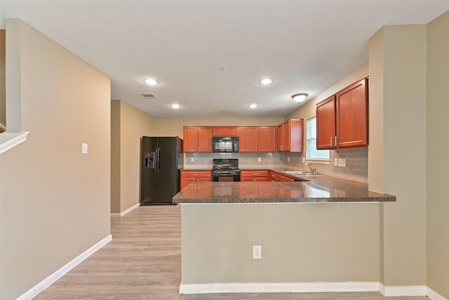 kitchen featuring a peninsula, a sink, brown cabinets, black appliances, and tasteful backsplash