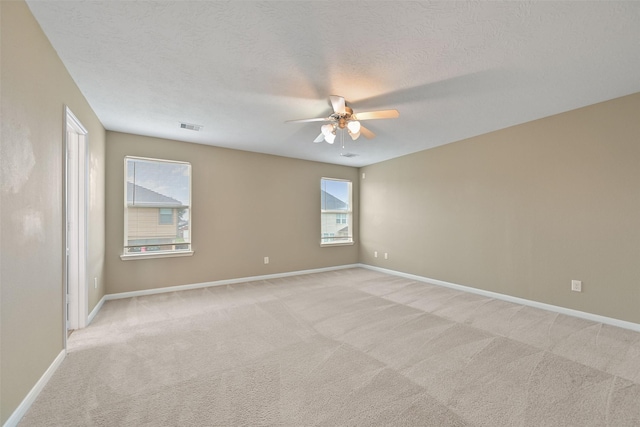 spare room with baseboards, visible vents, a ceiling fan, light colored carpet, and a textured ceiling