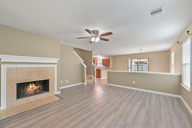 unfurnished living room featuring light wood finished floors, visible vents, a tiled fireplace, a textured ceiling, and baseboards