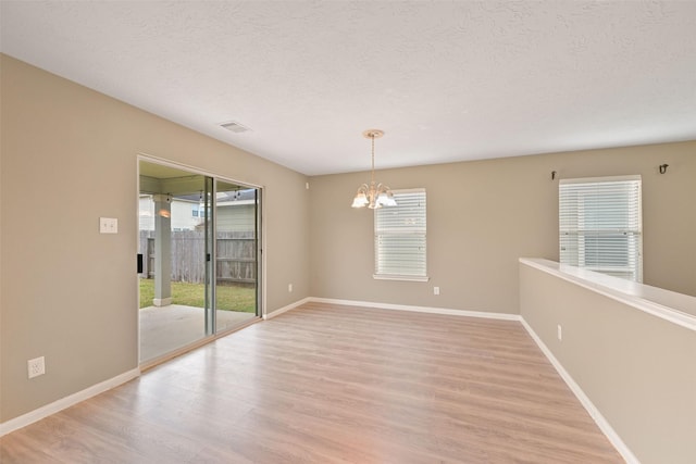 spare room featuring a chandelier, a wealth of natural light, light wood-type flooring, and visible vents