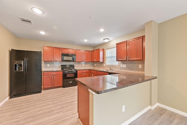 kitchen featuring visible vents, light wood-style floors, a peninsula, black appliances, and a sink