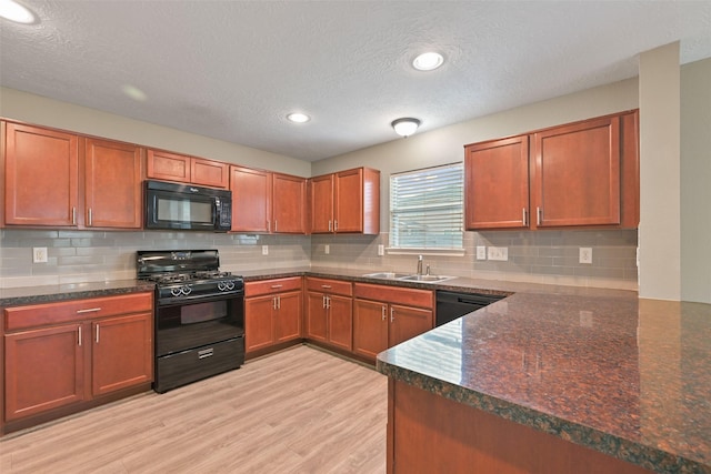 kitchen featuring dark stone countertops, a peninsula, light wood-type flooring, black appliances, and a sink