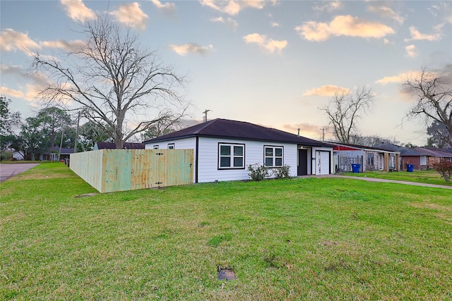 view of front of home featuring fence, a lawn, driveway, and a garage