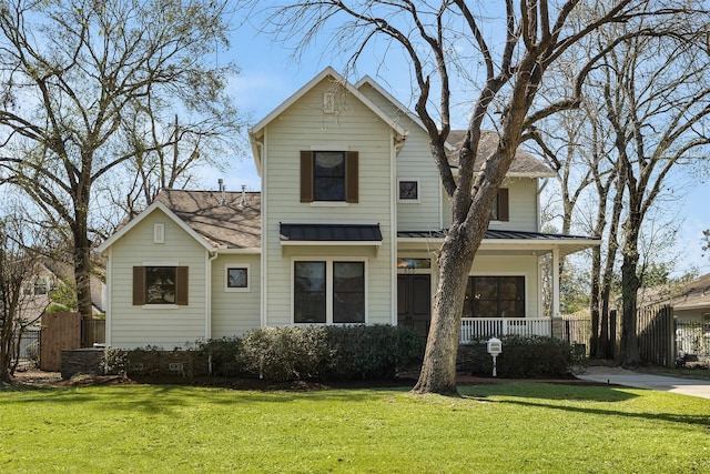 traditional-style house featuring a front lawn, a standing seam roof, a porch, and fence