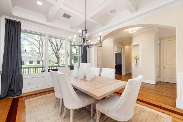 dining room with arched walkways, coffered ceiling, beamed ceiling, crown molding, and light wood-type flooring