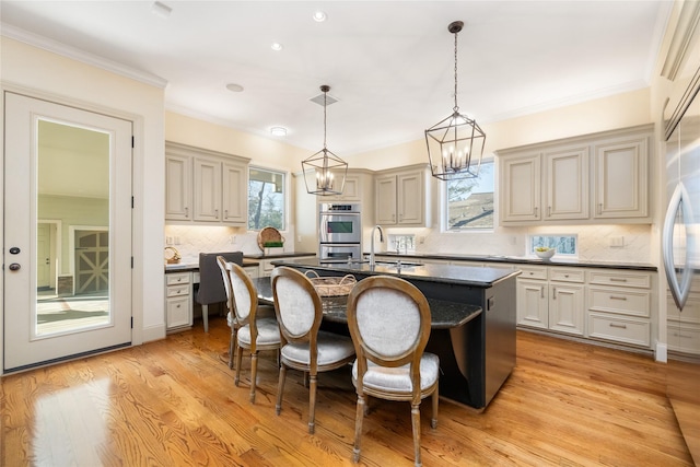 kitchen with a breakfast bar, hanging light fixtures, double oven, light wood-style floors, and a kitchen island with sink