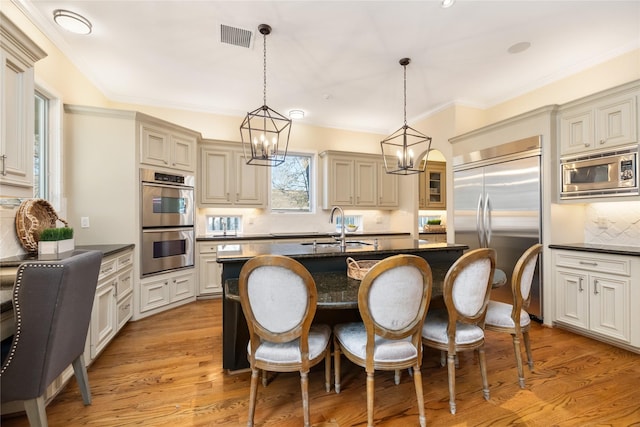 kitchen with a kitchen island with sink, decorative light fixtures, and built in appliances