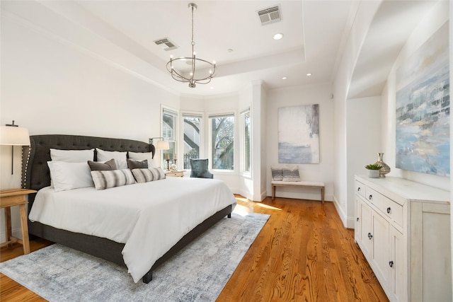 bedroom featuring light wood-style floors, baseboards, visible vents, and a raised ceiling